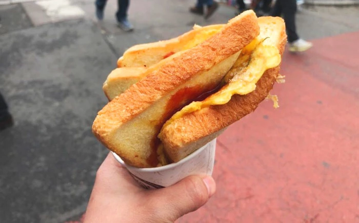 alguém segurando um toast coreano numa rua movimentada pela manhã