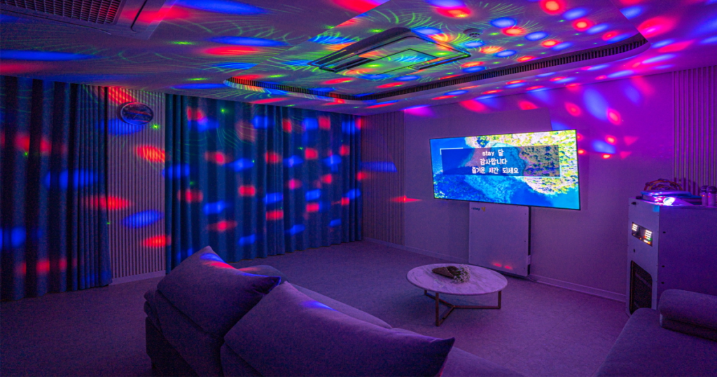 Interior de una sala de noraebang coreano con micrófonos, pantalla grande y sofás