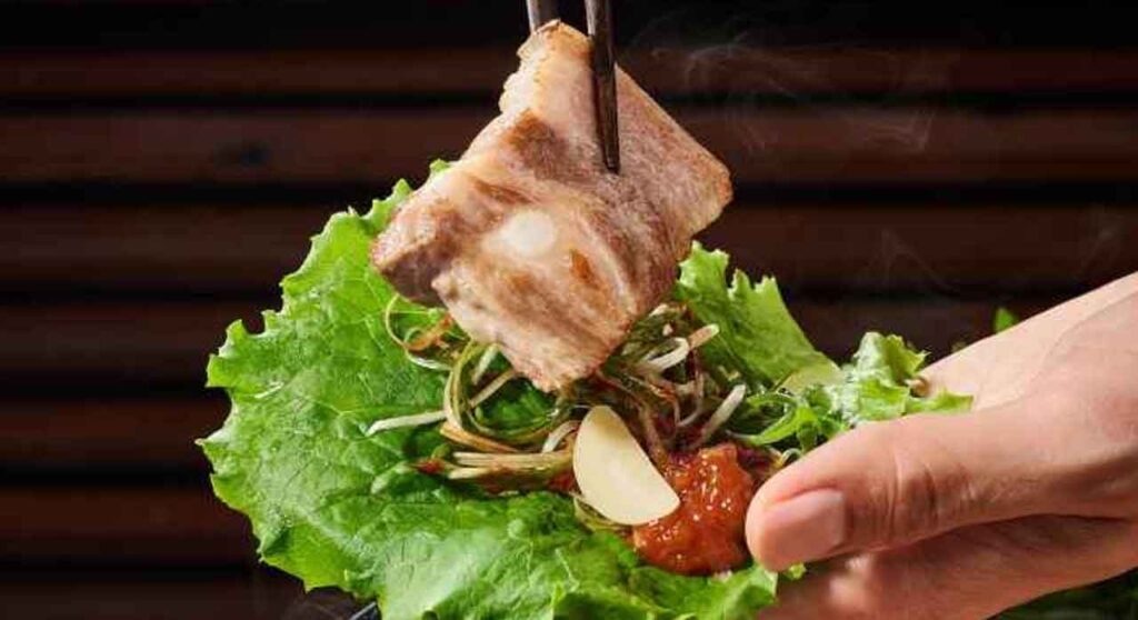 Hand making a lettuce wrap with grilled meat and ssamjang at Korean BBQ
