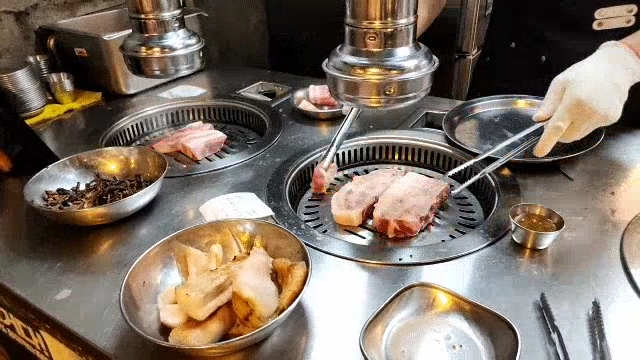 Grilling samgyeopsal with tongs at a Korean BBQ restaurant