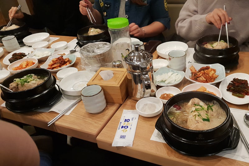 Samgyetang servido con platos de acompañamiento coreanos sobre una mesa de restaurante.