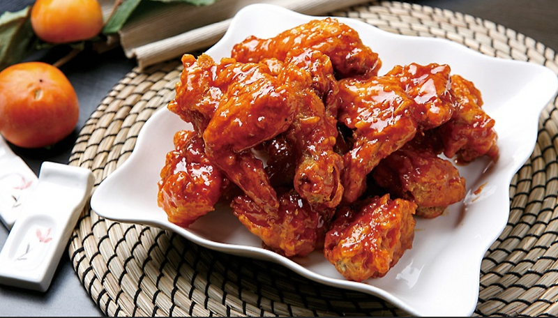 Primer plano de pollo frito coreano cubierto con una salsa roja brillante